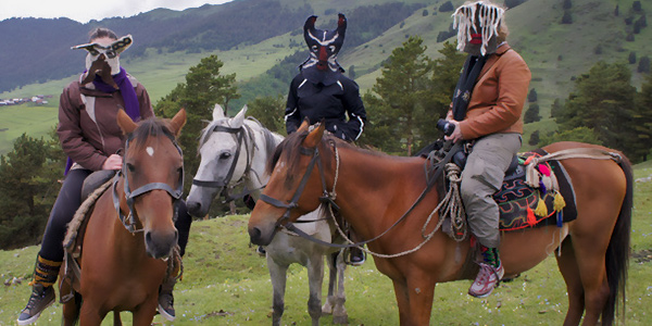three artists wearing felt masks on horseback in a mountain setting